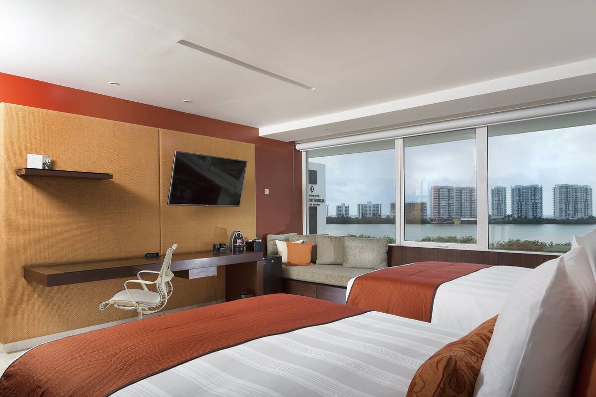 A modern hotel room with a city view, a sofa, a desk, and a bed.