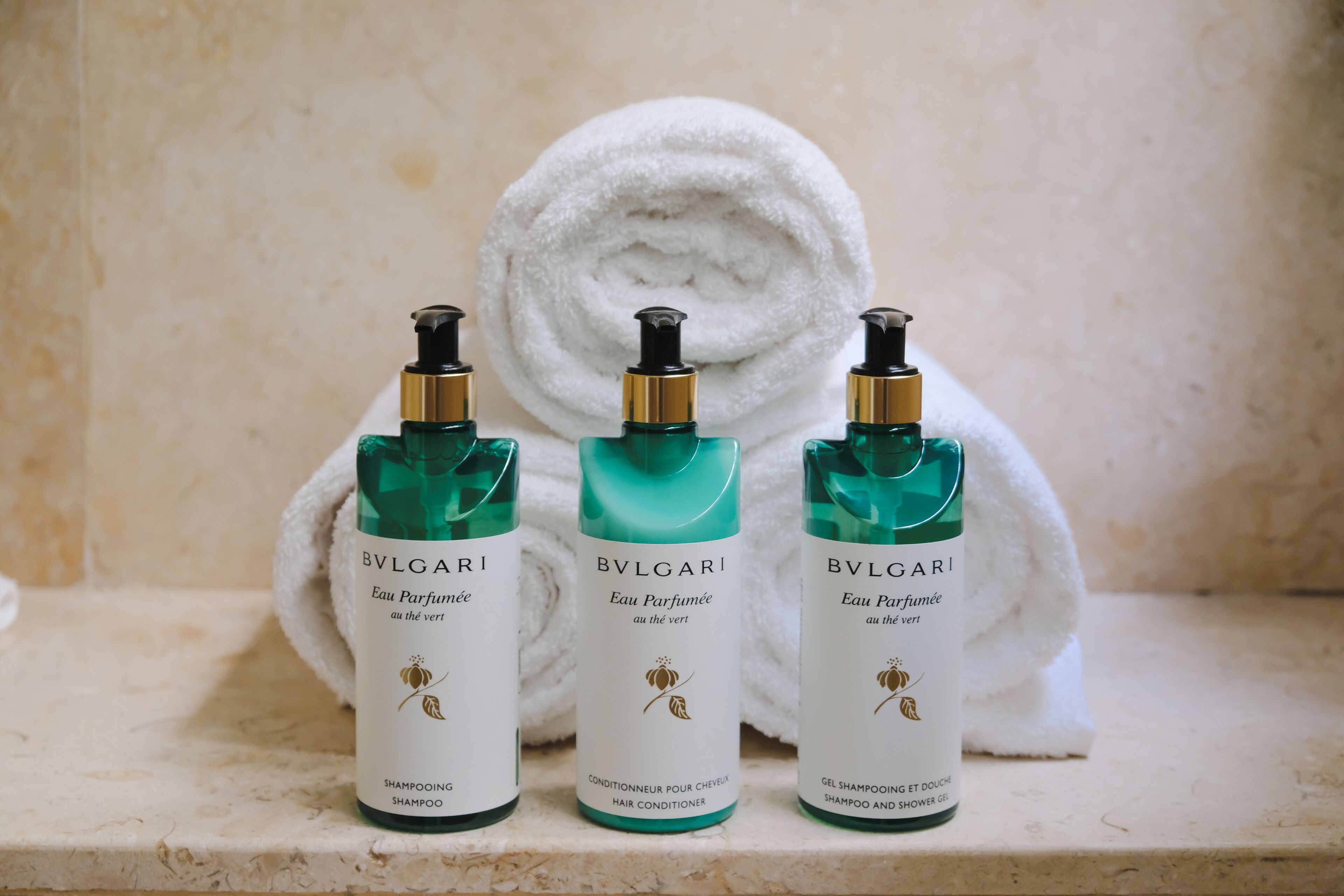 Tres botellas de Eau de Parfum BVLGARI sobre una superficie de mármol con una toalla blanca al fondo.