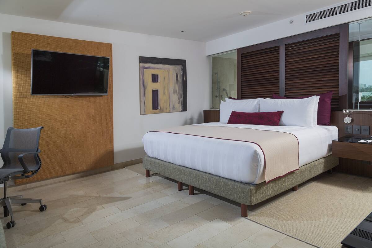 A modern hotel room with a large bed, a desk, a chair, and a television mounted on the wall.