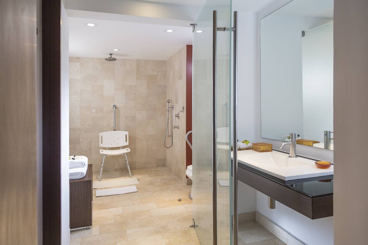 A modern bathroom with a glass shower enclosure, a white sink with a dark countertop, and a large mirror.