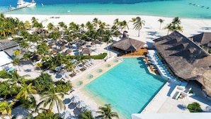 Vista aérea de un resort con una piscina grande, playa y edificios de techo de paja.