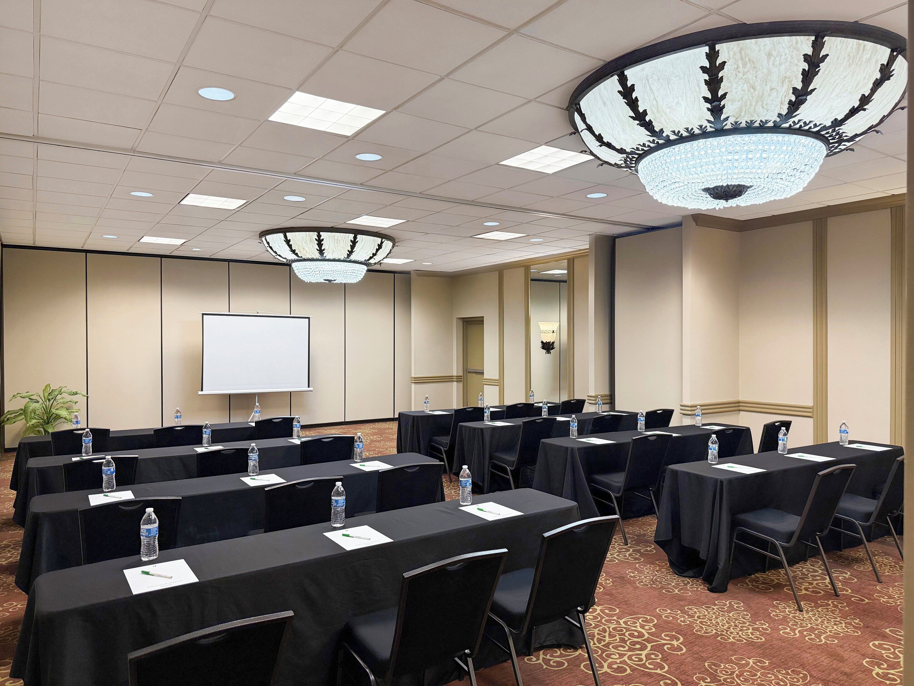 A conference room with multiple tables, chairs, water bottles, and a projector screen.
