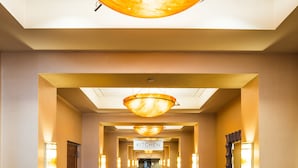 Un couloir d’hôtel avec un tapis à motifs, des appliques murales et un panneau indiquant la direction de la cuisine.