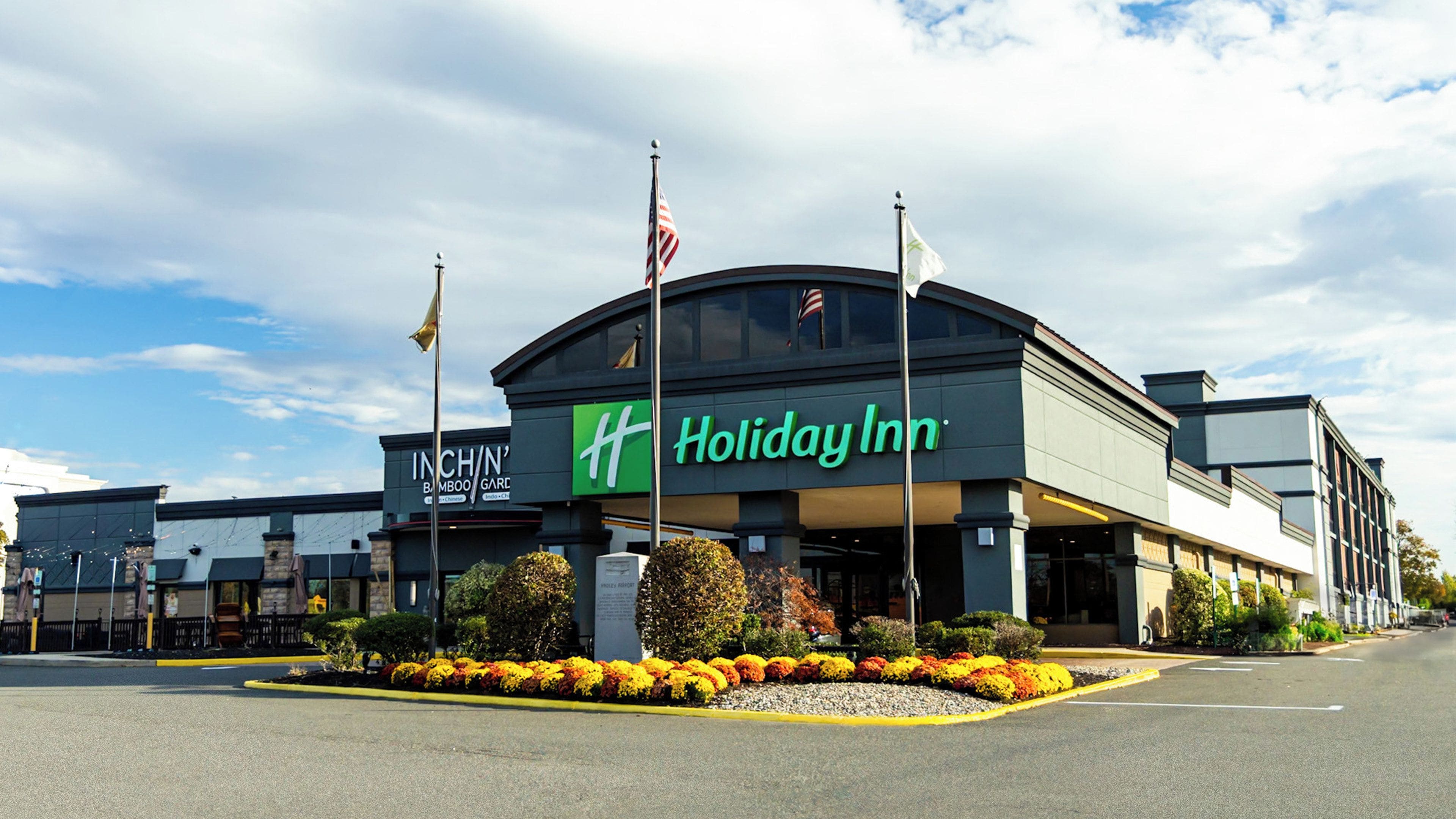 A Holiday Inn hotel with a large sign, flags, and a landscaped area with flowers.