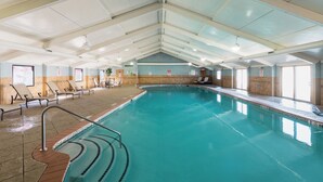 Une piscine intérieure à l’eau claire, avec des murs carrelés et un plafond laissant apparaître les conduits de ventilation.