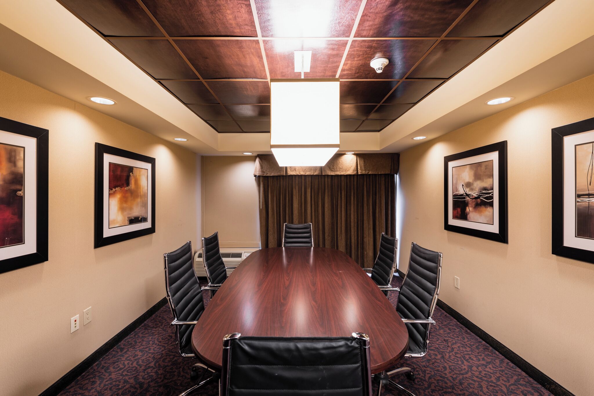 A conference room with a large wooden table, six black chairs, and framed artwork on the walls.