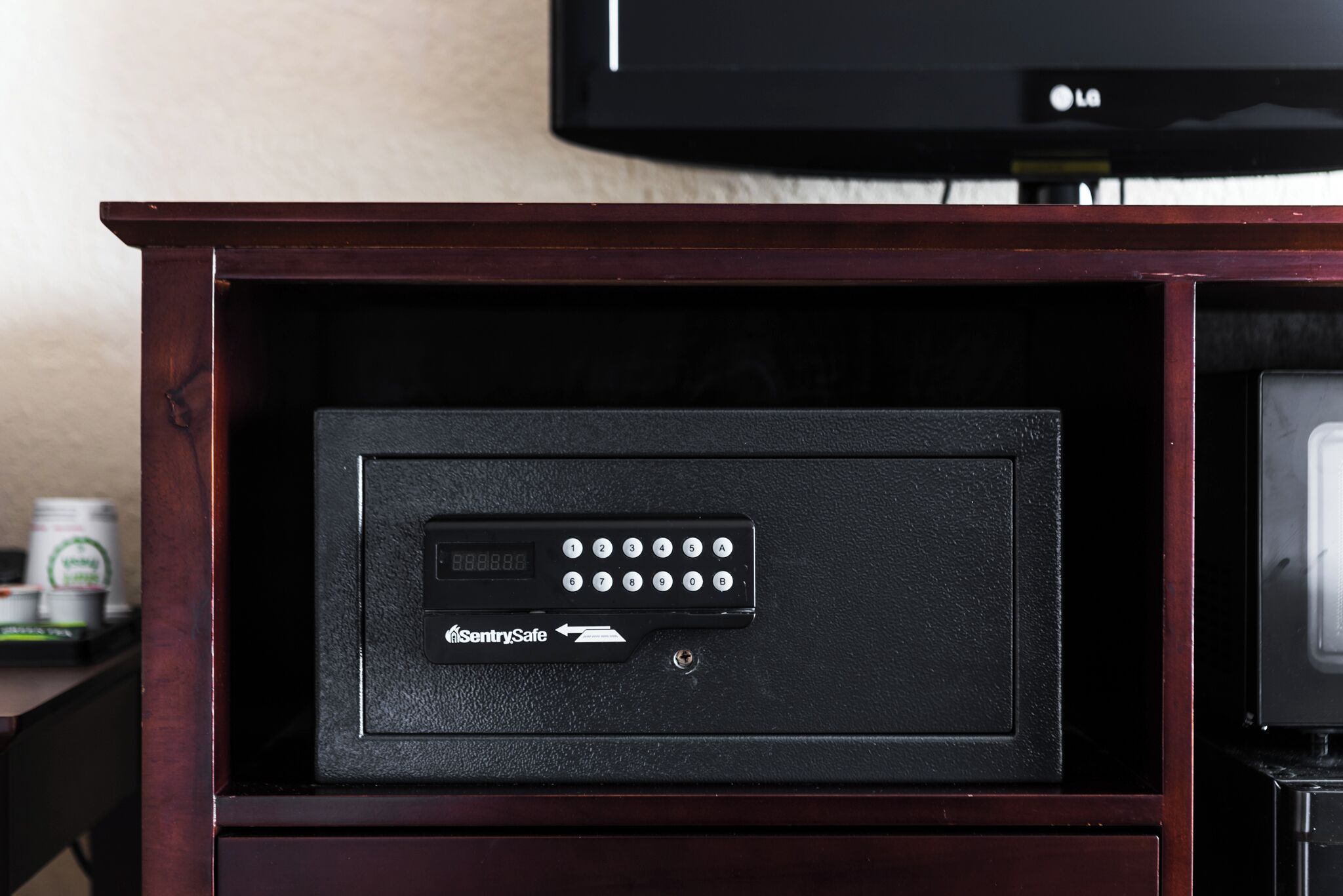 Et pengeskab med et tastatur og et "SentrySafe" logo, placeret i et træskab.