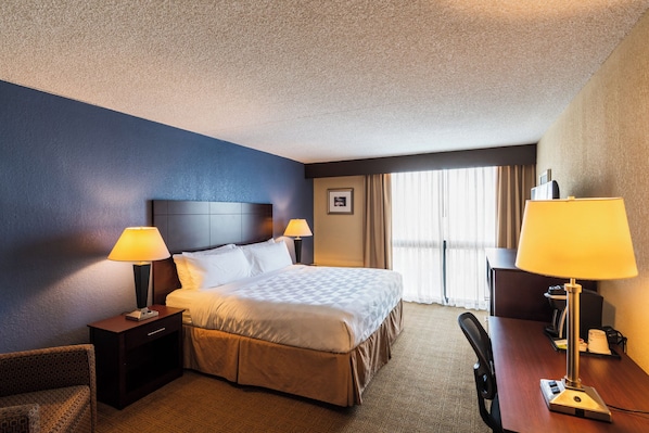 A hotel room with a bed, two bedside tables with lamps, a desk with a chair, and a large window with curtains. - Holiday Inn South Plainfield-Piscataway by IHG (South Plainfield)