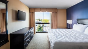Une chambre d’hôtel avec un grand lit, une commode, une télévision et un balcon offrant une vue sur la ville.