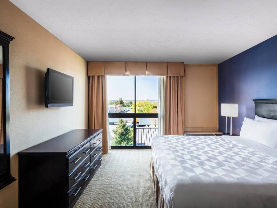A hotel room with a large bed, a dresser, a TV, and a balcony with a view of the city.
