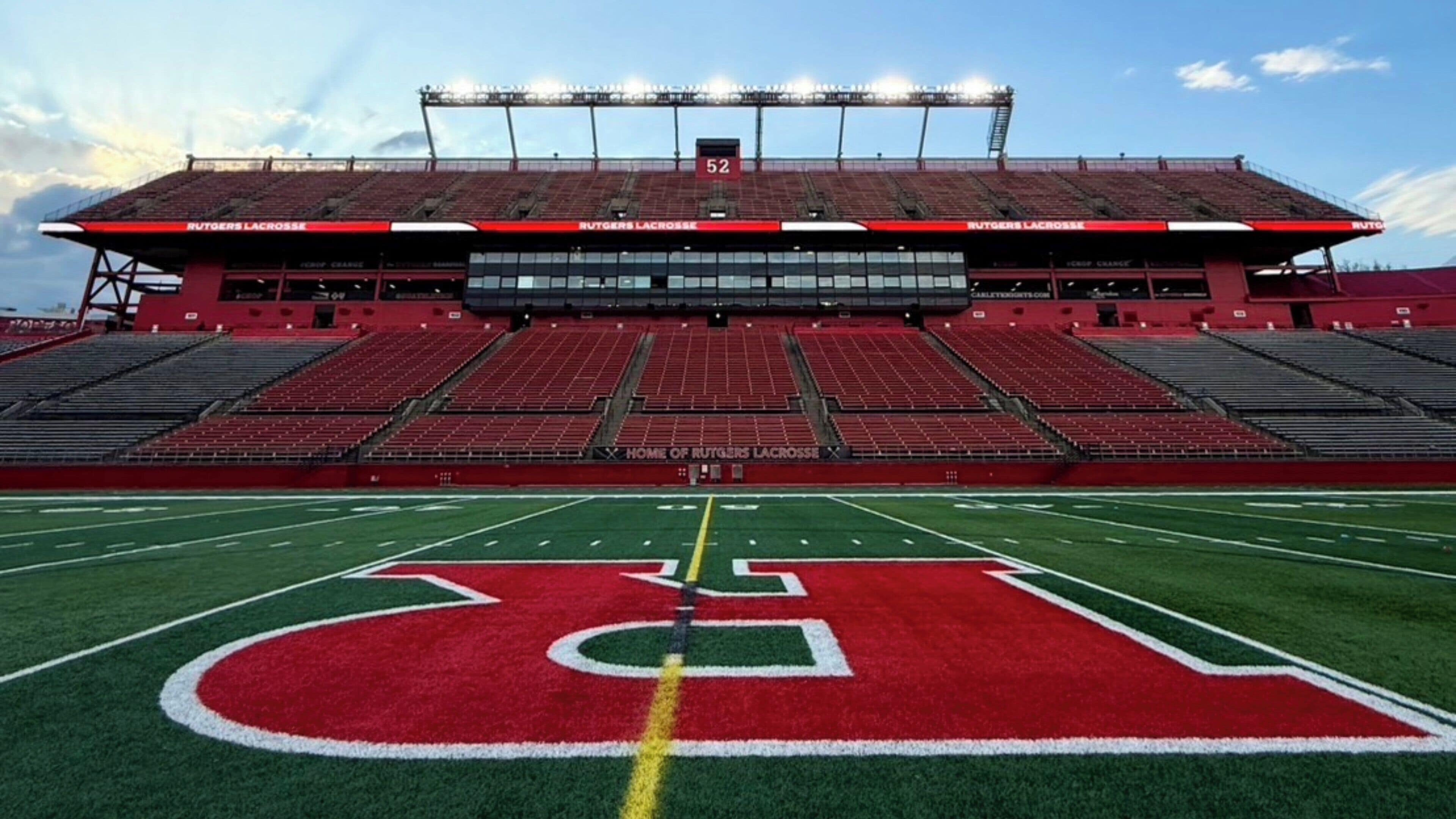 An empty stadium with a football field, marked with a large "D" logo, and a scoreboard displaying the number 52.