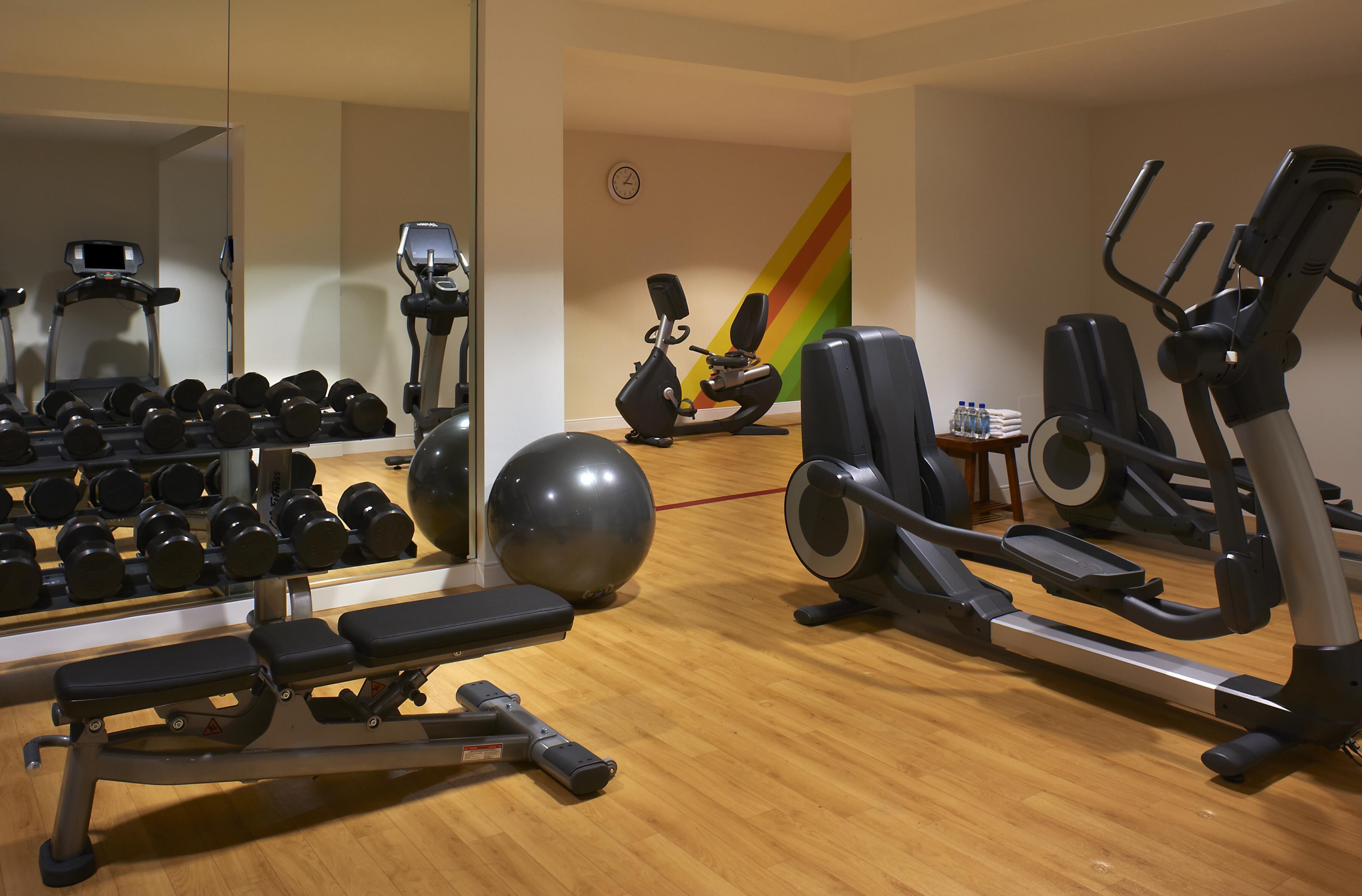 A gym with exercise equipment, a mirror, and a clock on the wall.
