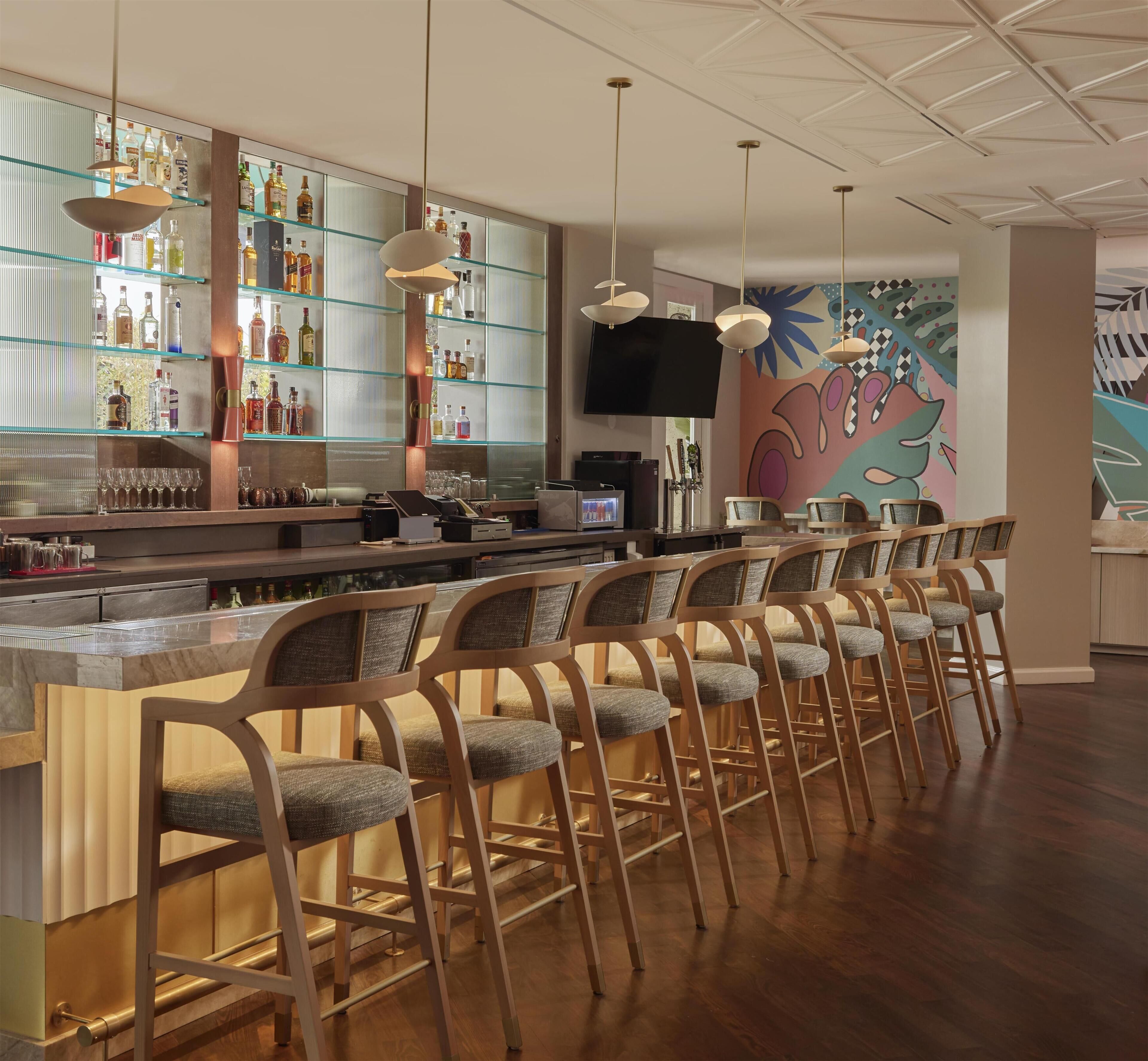 A bar area with a long counter, multiple bar stools, and a variety of liquor bottles.