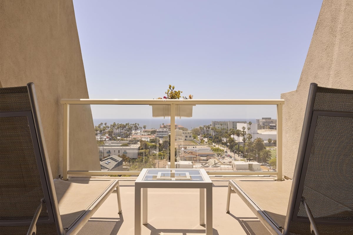 A balcony with a table and chairs, offering a view of a cityscape and the ocean.