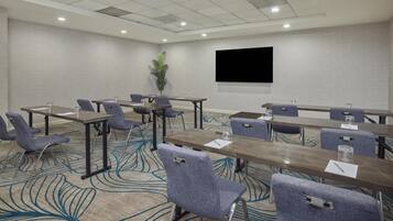 A conference room with tables, chairs, a flat-screen TV, and a patterned carpet.