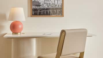 Una habitación con un escritorio blanco, una lámpara rosa, una silla y un cuadro en la pared.
