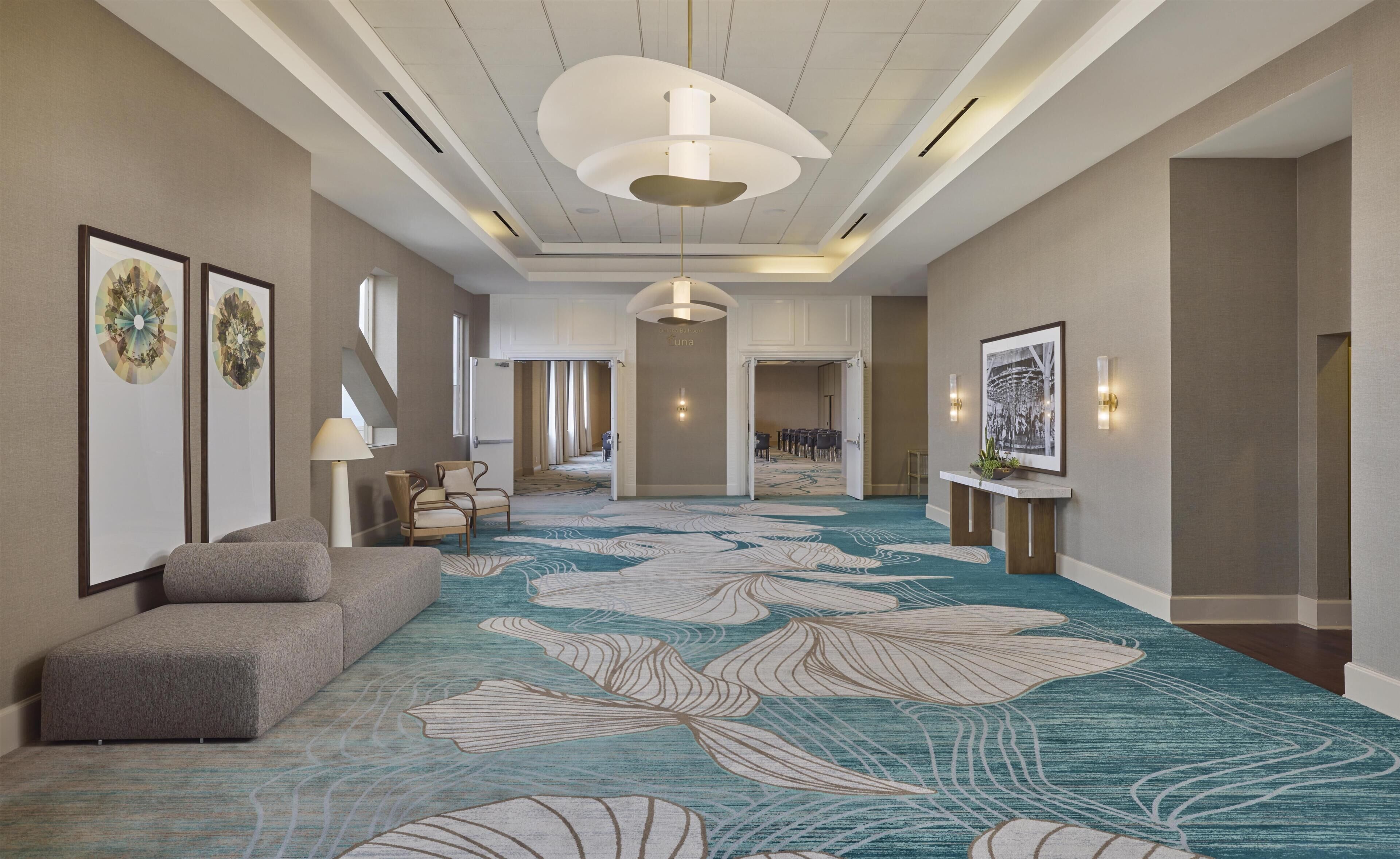 A hotel lobby with a patterned carpet, seating area, framed artwork, and a reception desk.