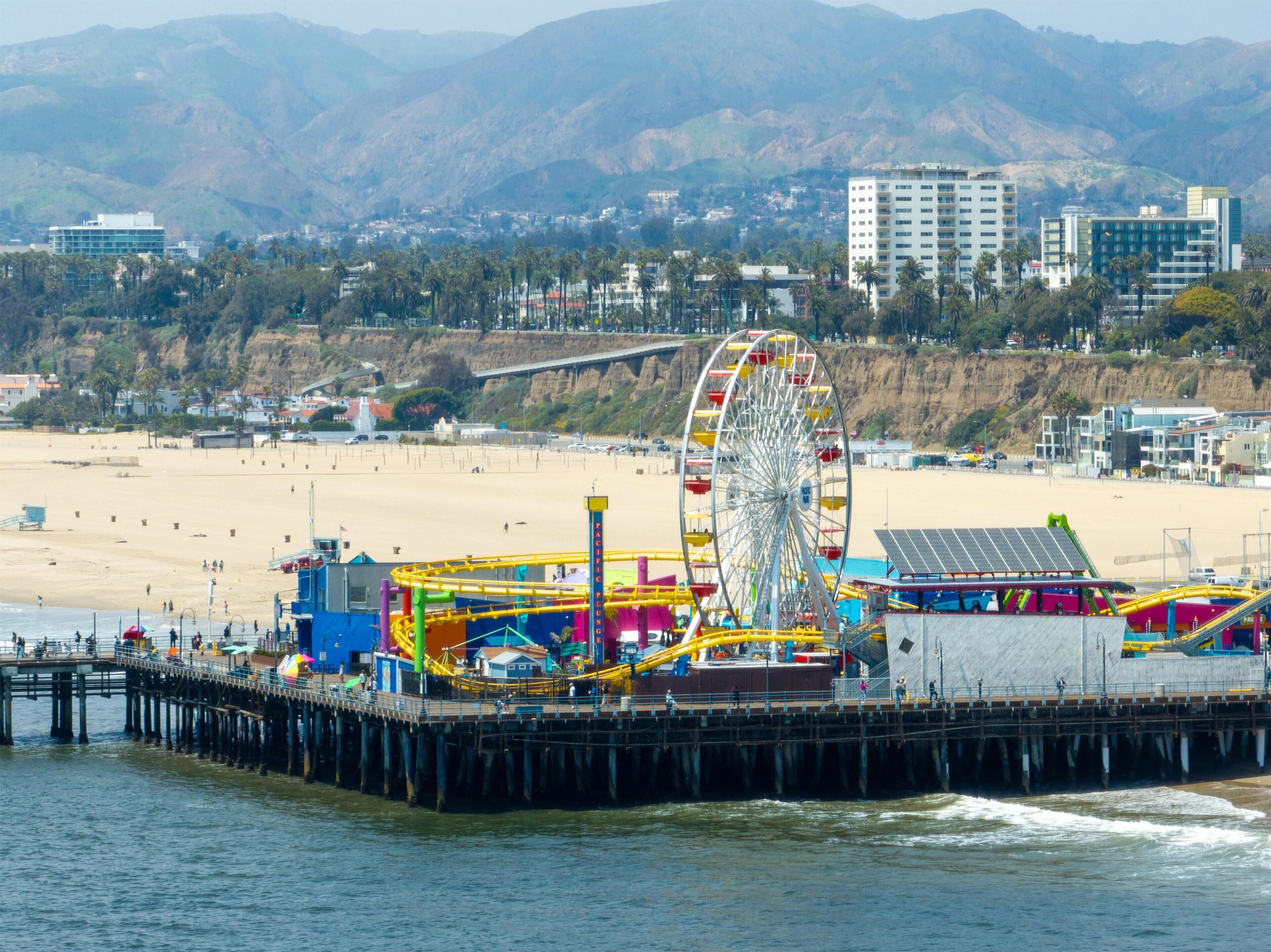 A pier with a Ferris wheel, beach, and buildings in the background.