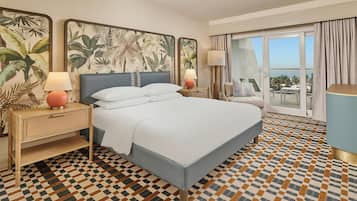 A hotel room with a large bed, two bedside tables with lamps, a view of the outdoors, and a patterned floor.