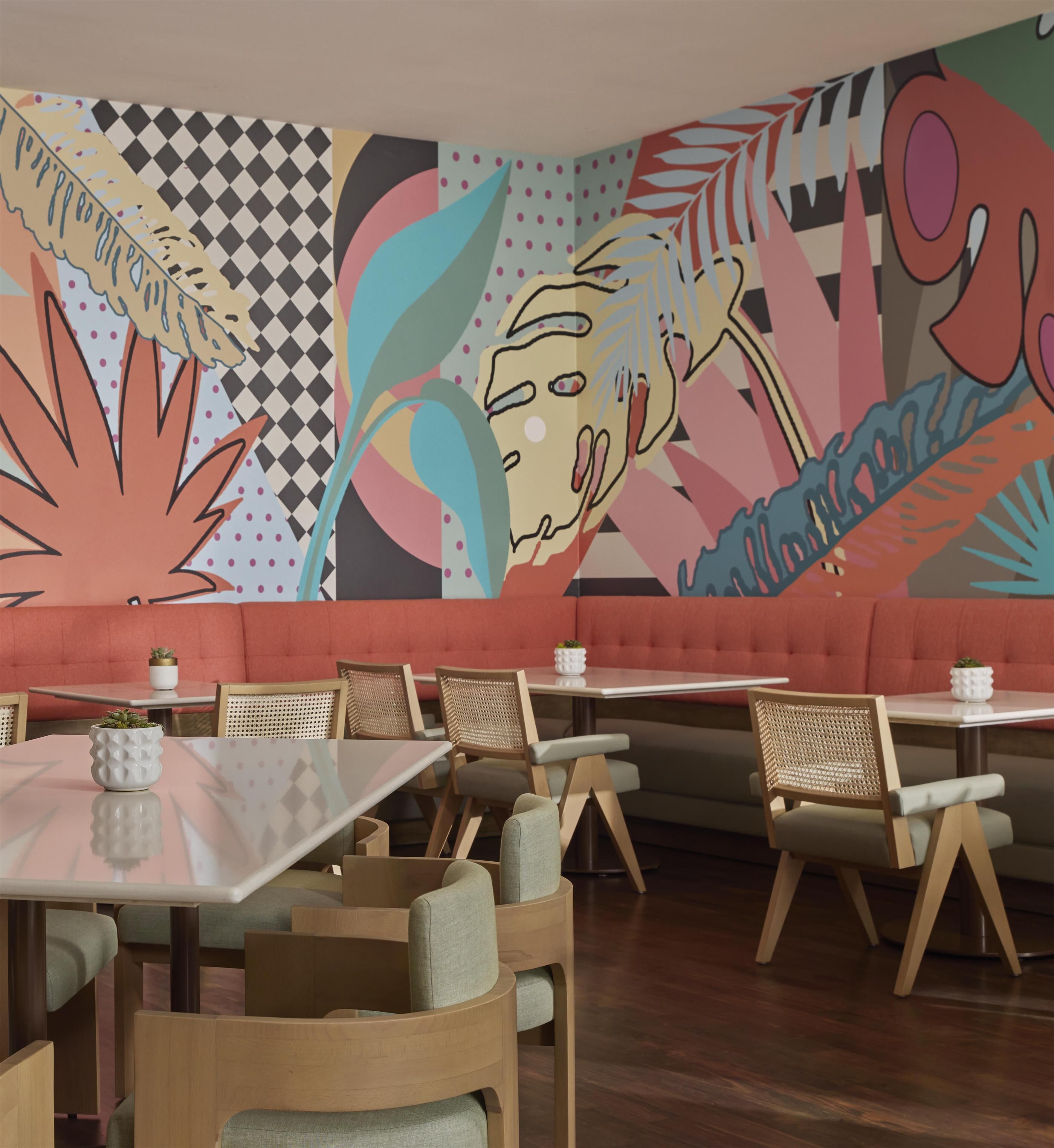 A restaurant interior with a modern design, featuring a large mural, cushioned seating, and wooden tables.
