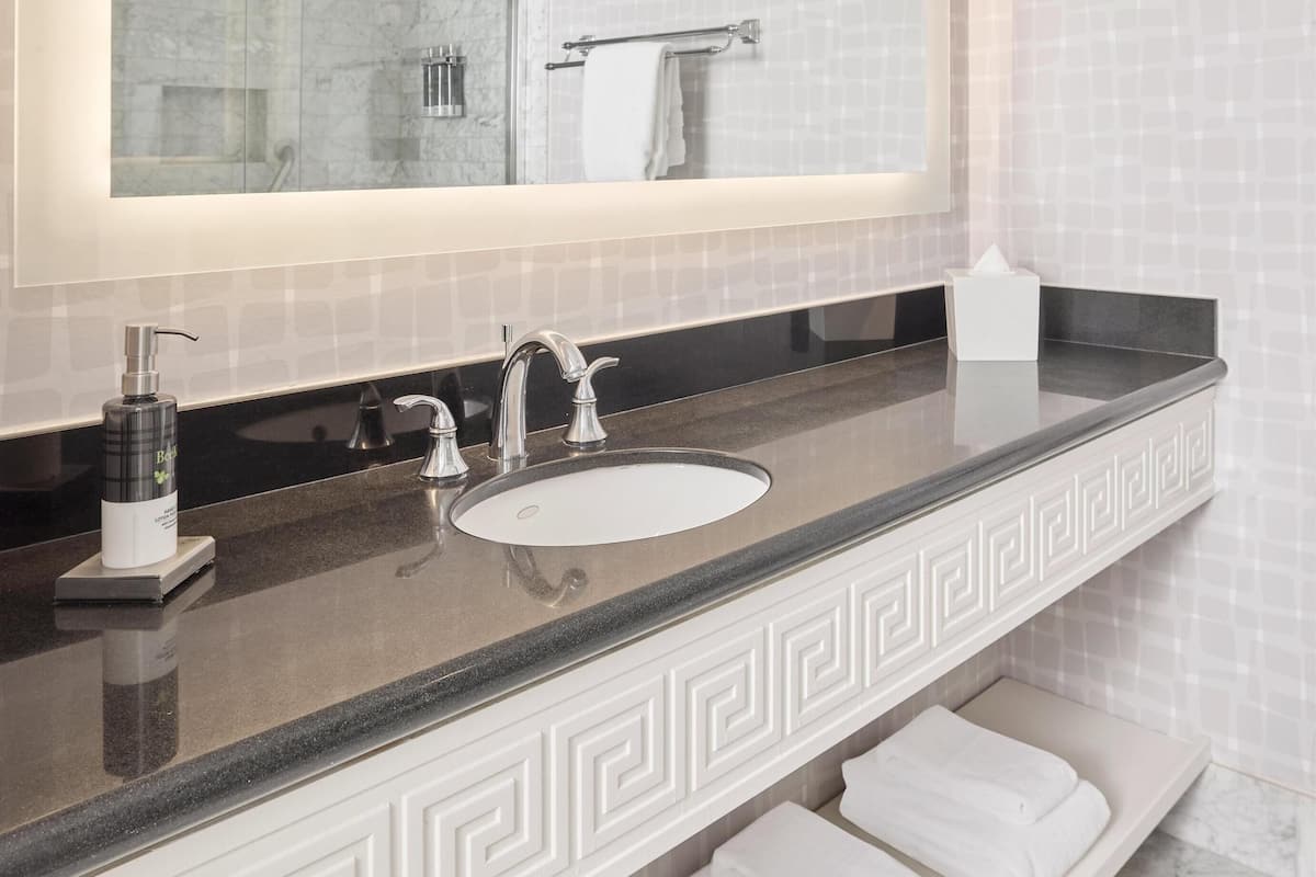 A bathroom with a large mirror, a sink, a towel rack, and a bottle of hand soap.