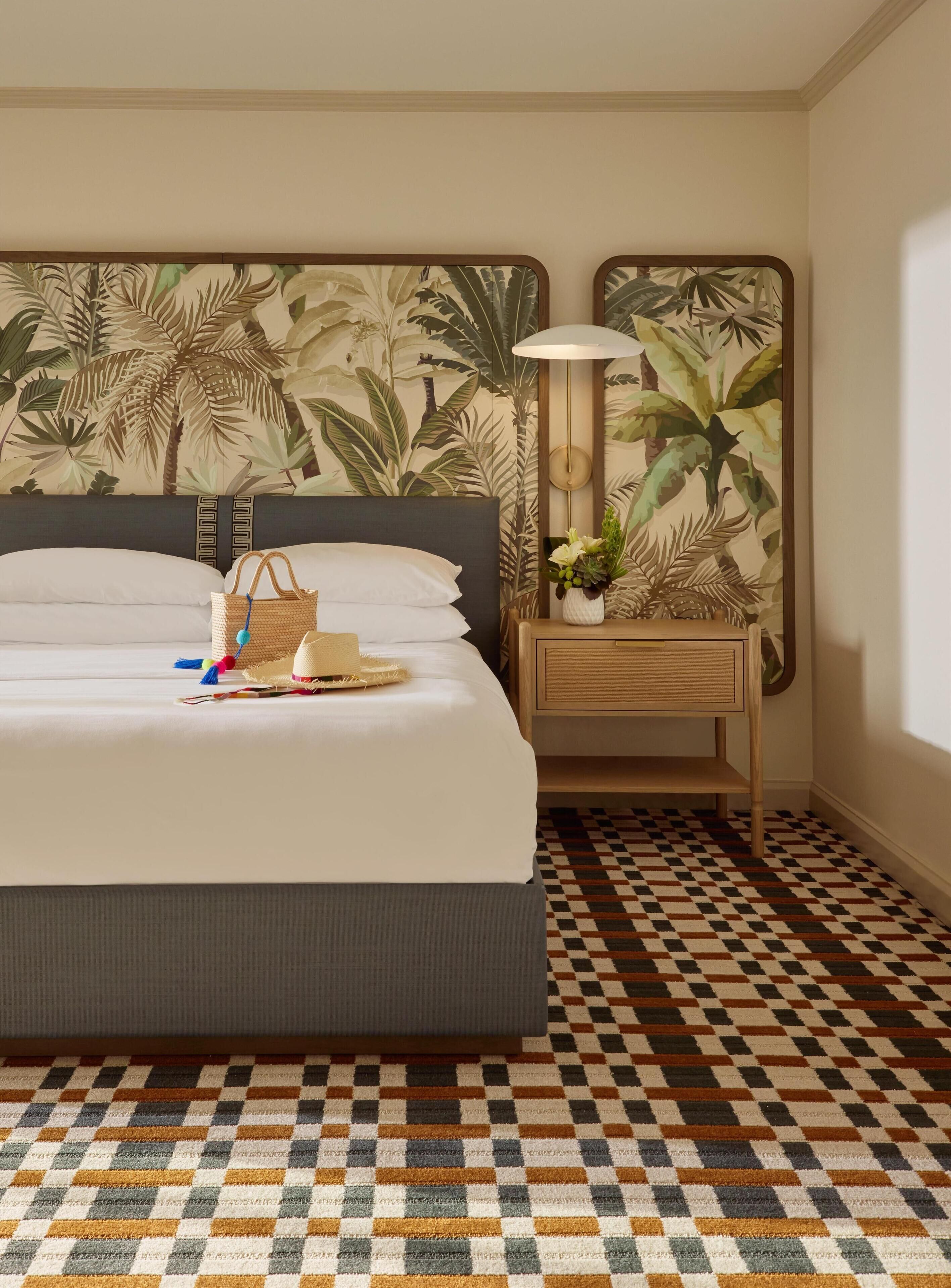 A hotel room with a bed, a nightstand with a lamp, a patterned wall, and a checkered floor.