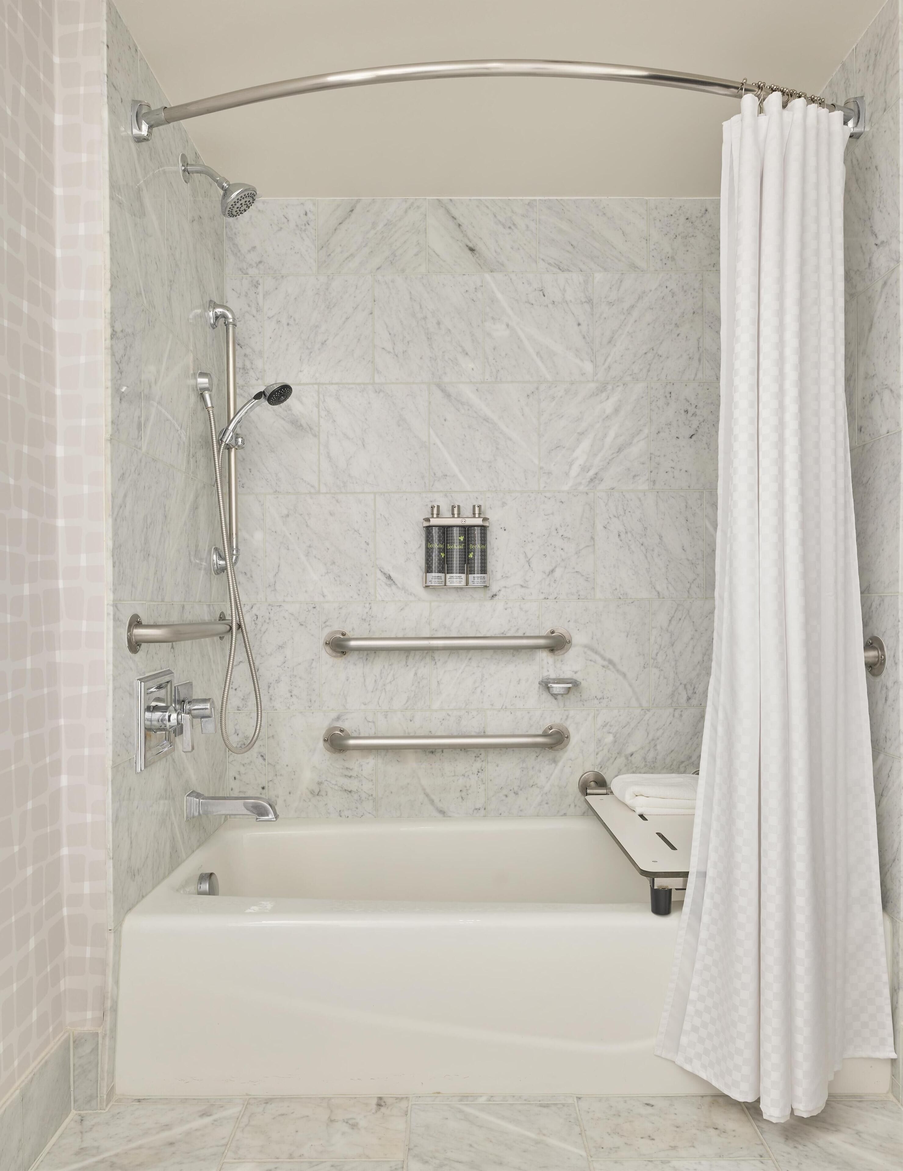 A modern bathroom with a bathtub, a shower with a handheld showerhead, grab bars, and a white shower curtain.