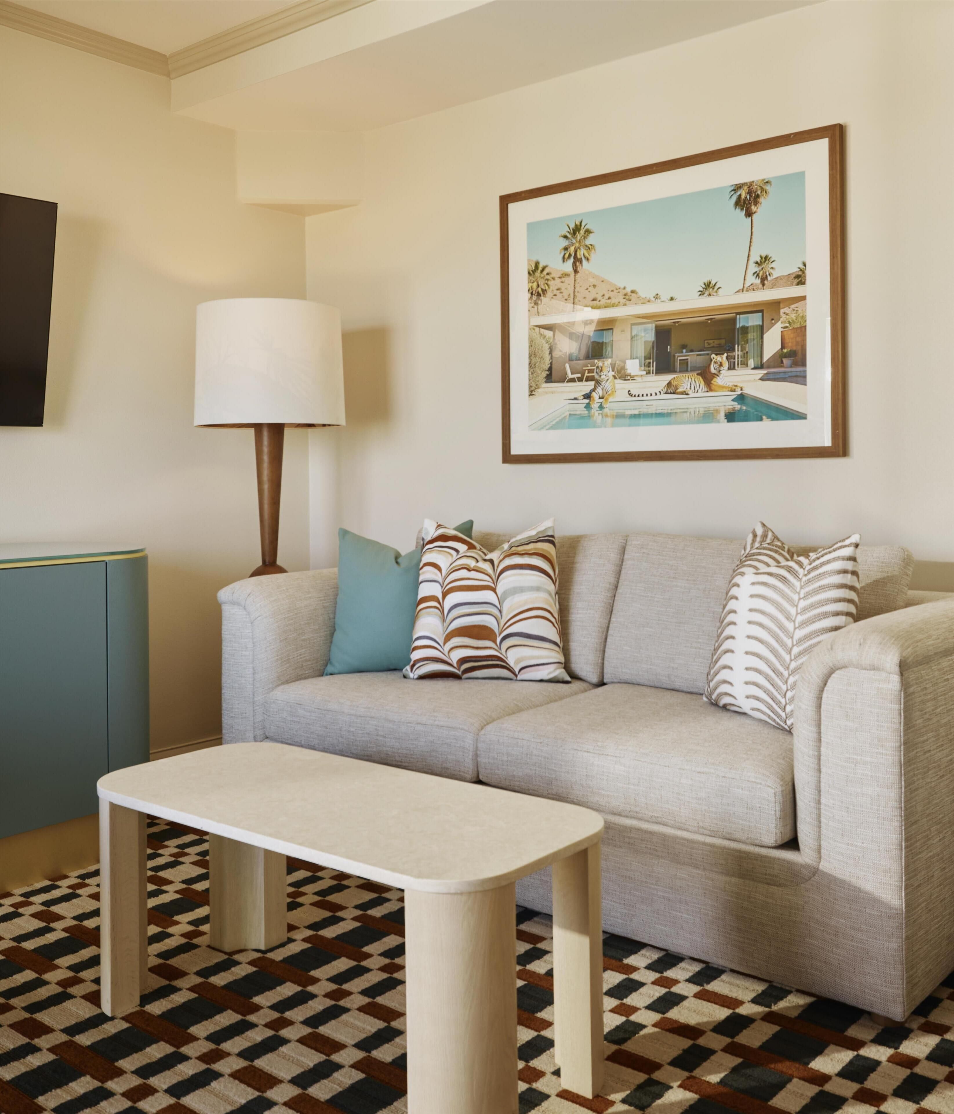Un salón con sofá, cojines, una mesa, una lámpara y un cuadro en la pared.