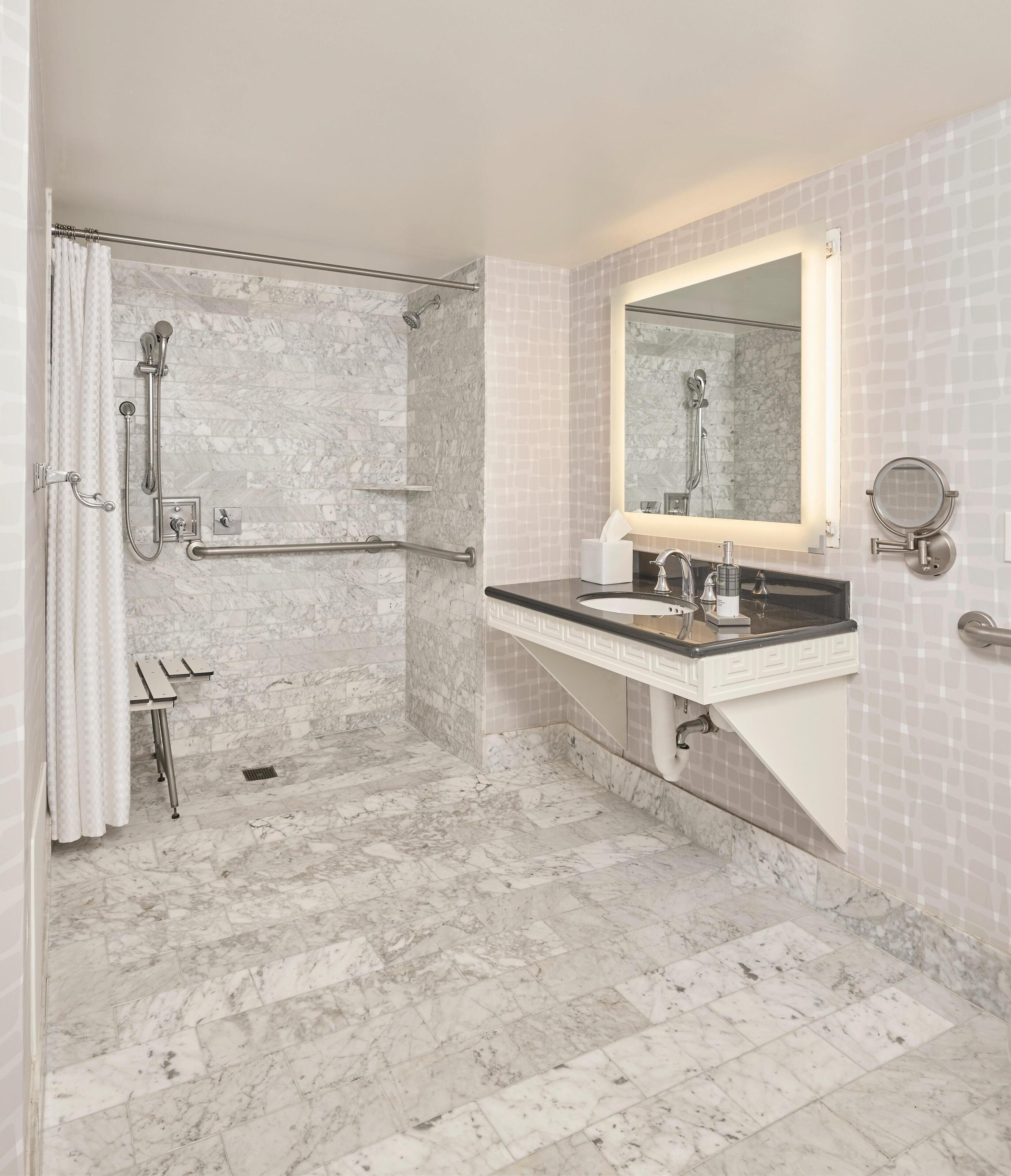 A bathroom with a shower, a sink, a mirror, and a handrail.