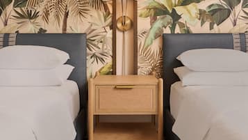 Una habitación con dos camas, una mesita de noche con lámpara y un papel tapiz con hojas tropicales.