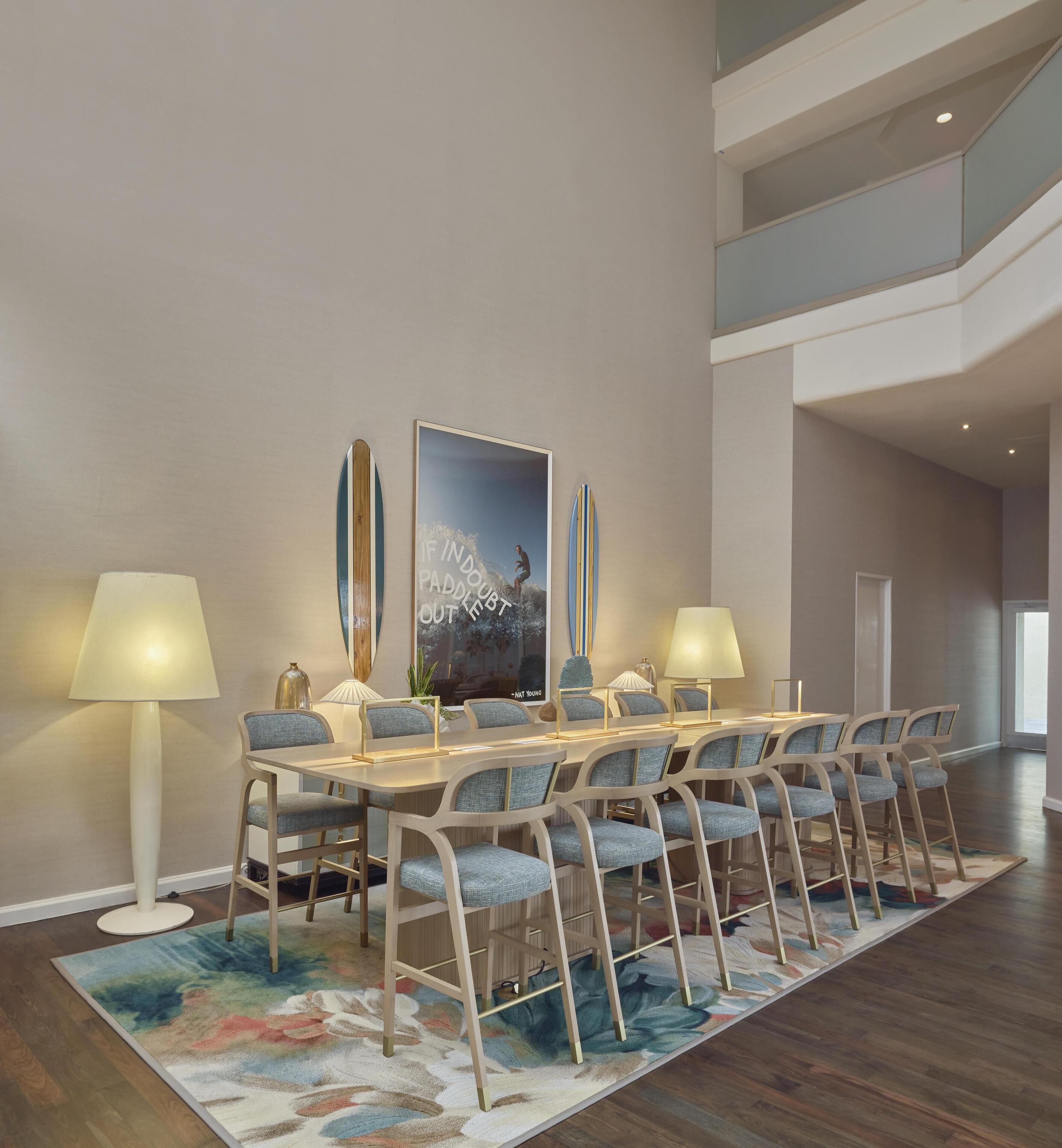A dining area with a long table, multiple chairs, two lamps, and a large poster on the wall.