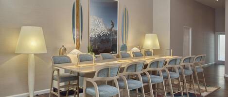 A dining area with a long table, multiple chairs, two lamps, and a large poster on the wall.
