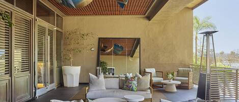 Un espacio lounge exterior moderno con un sofá de madera, mesas redondas y un techo con diseño de cuadrícula.
