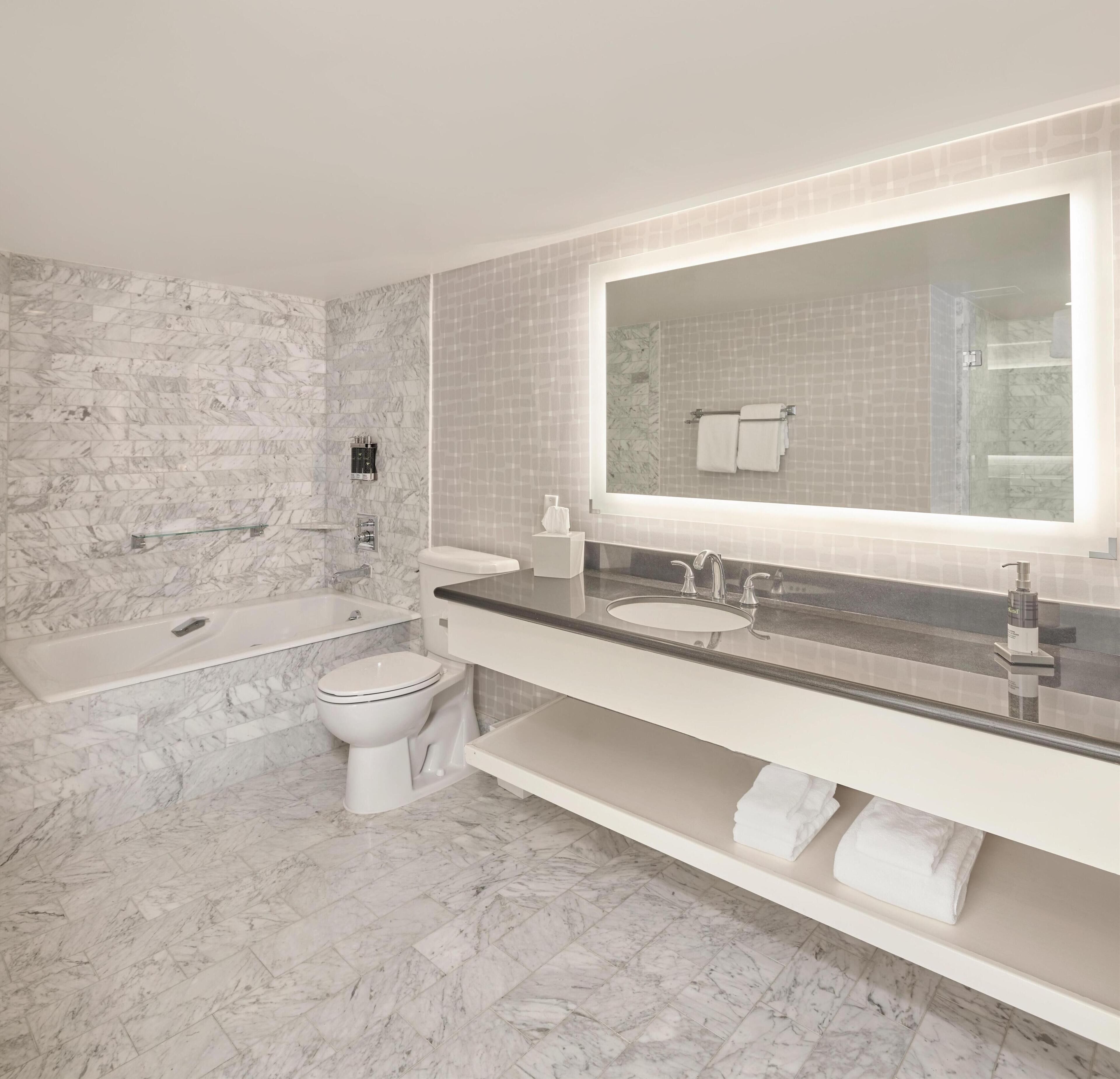 Une salle de bain avec un sol en marbre, une baignoire, des toilettes, un lavabo avec un grand miroir et un porte-serviettes.