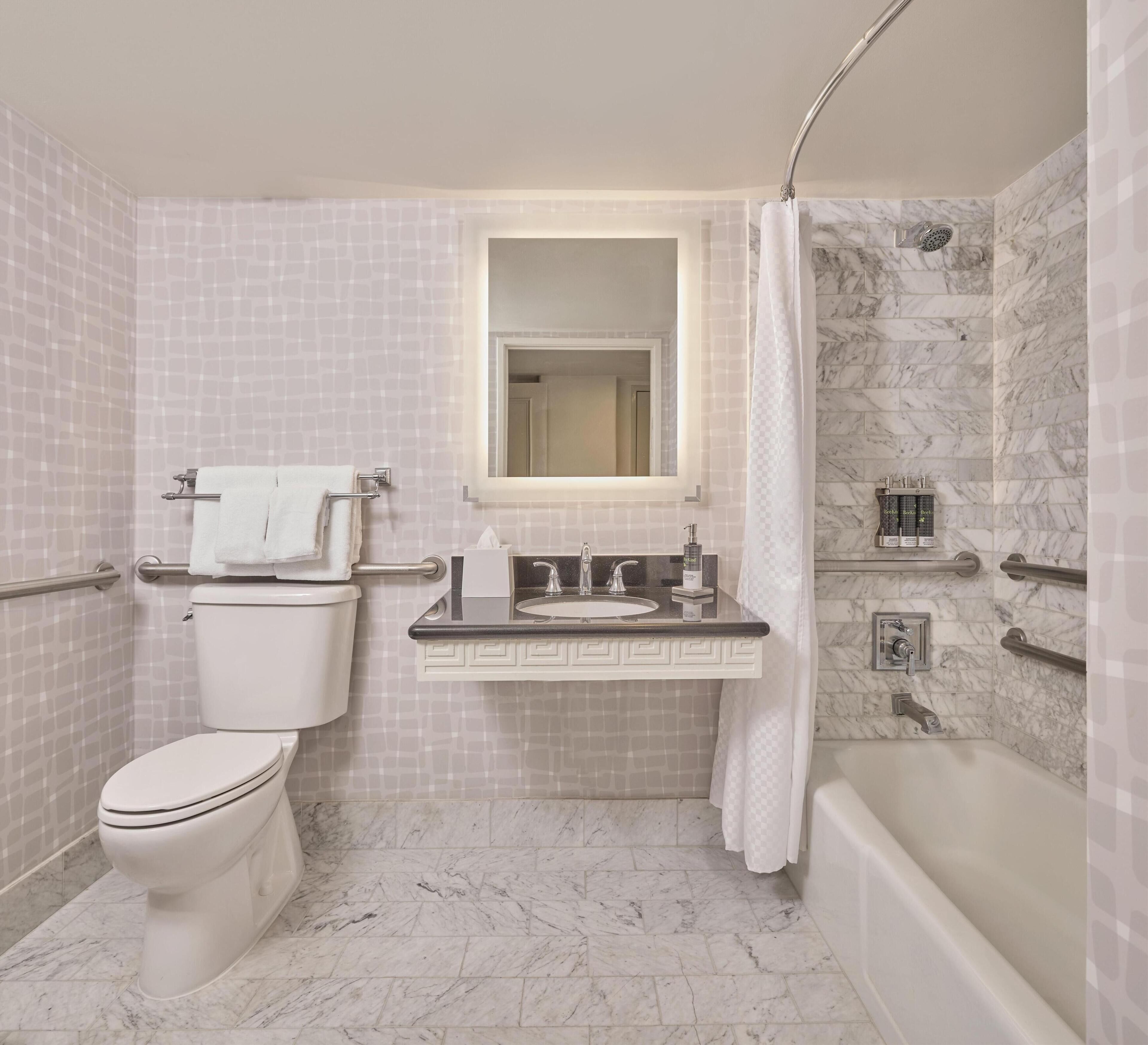 A bathroom with a toilet, sink, mirror, shower, and marble tiles.