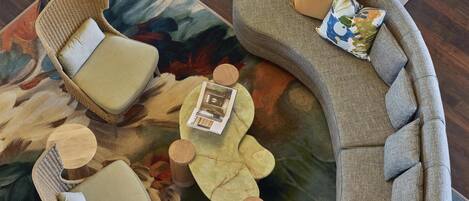 Una sala de estar moderna con un sofá gris curvo, sillas de mimbre, una mesa de centro y un tapete estampado.