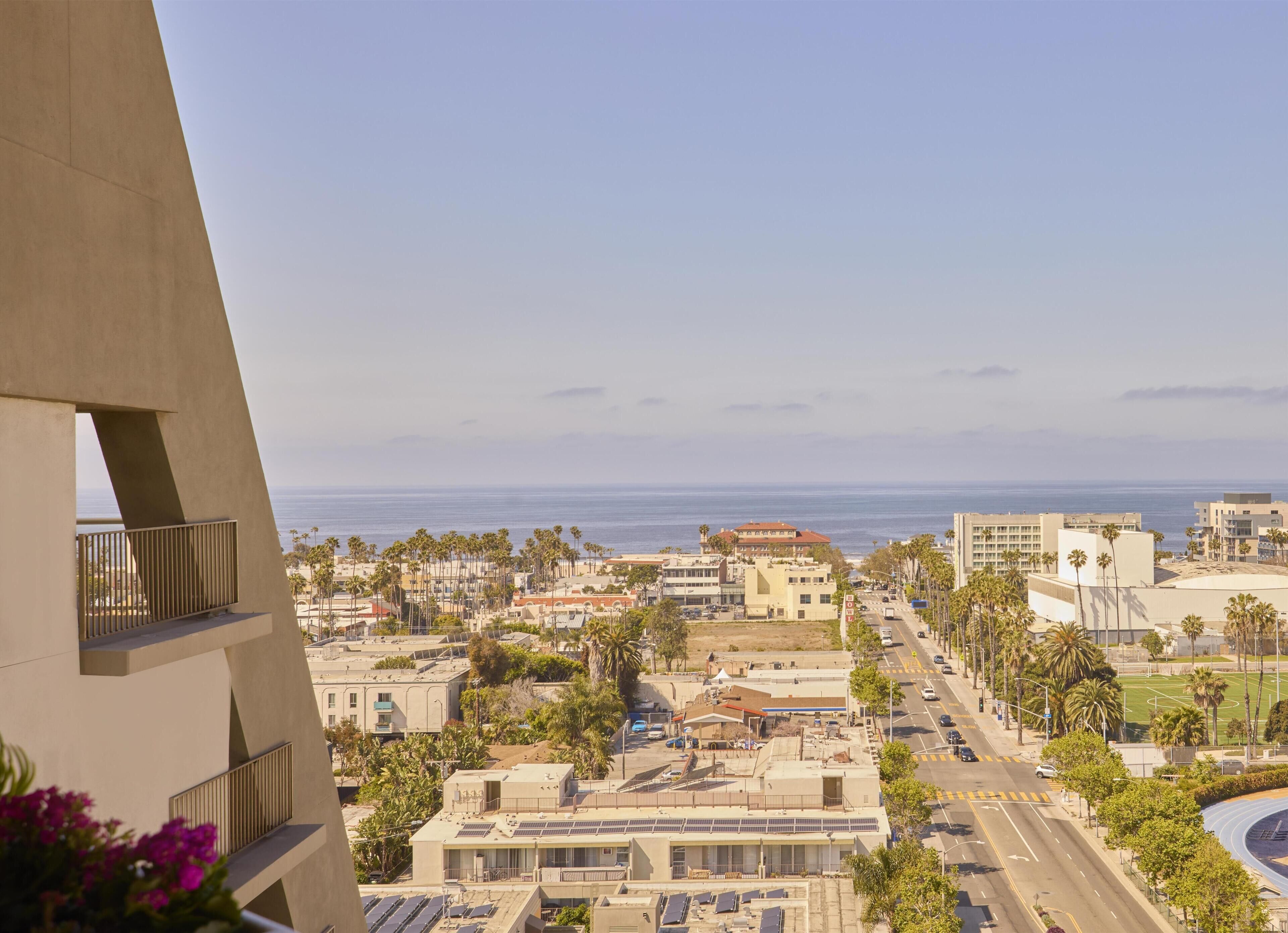 A coastal cityscape with a view of the ocean, buildings with solar panels, and a road with palm trees.