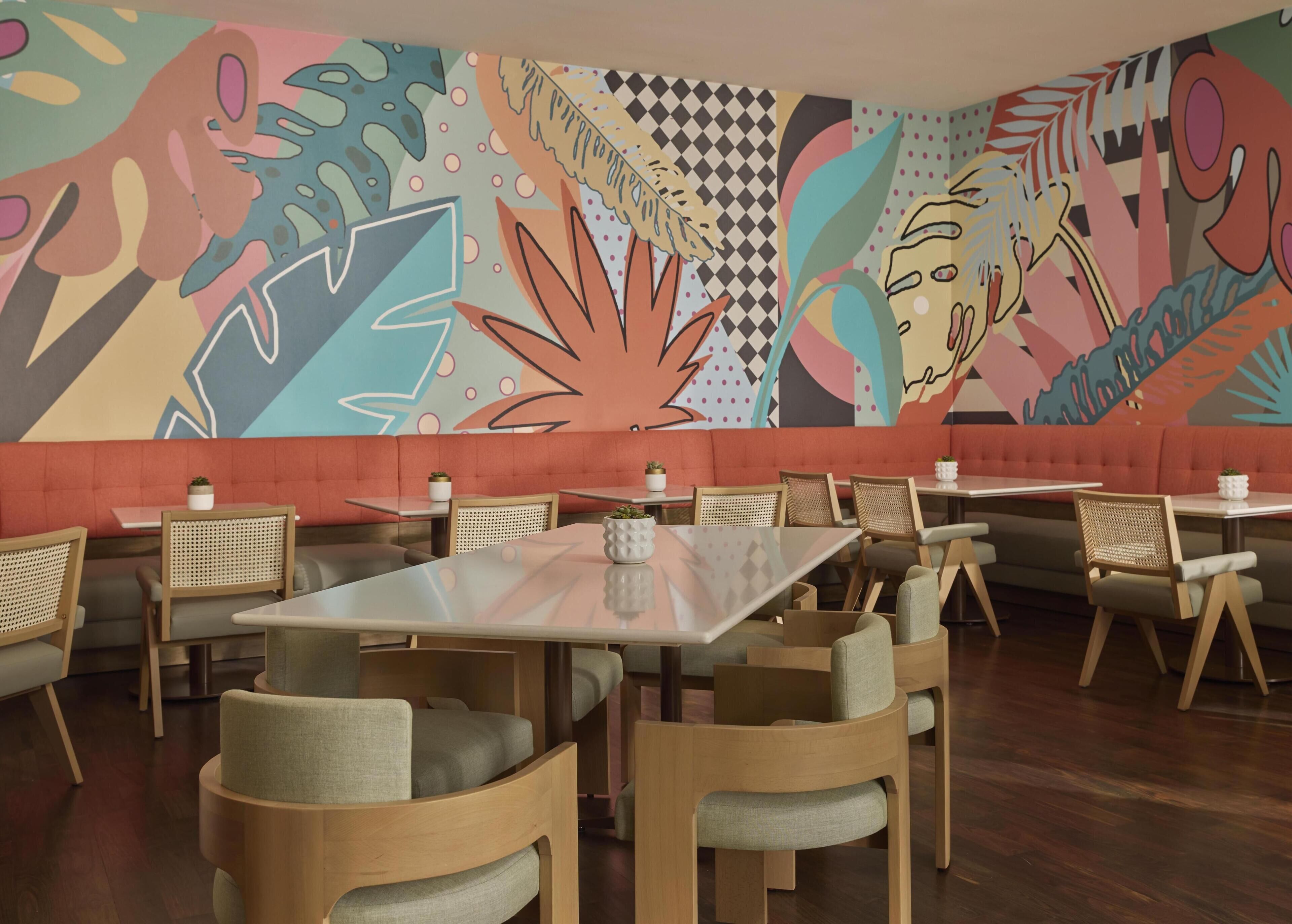 A restaurant interior with booths, tables, and chairs, featuring a colorful abstract mural on the wall.