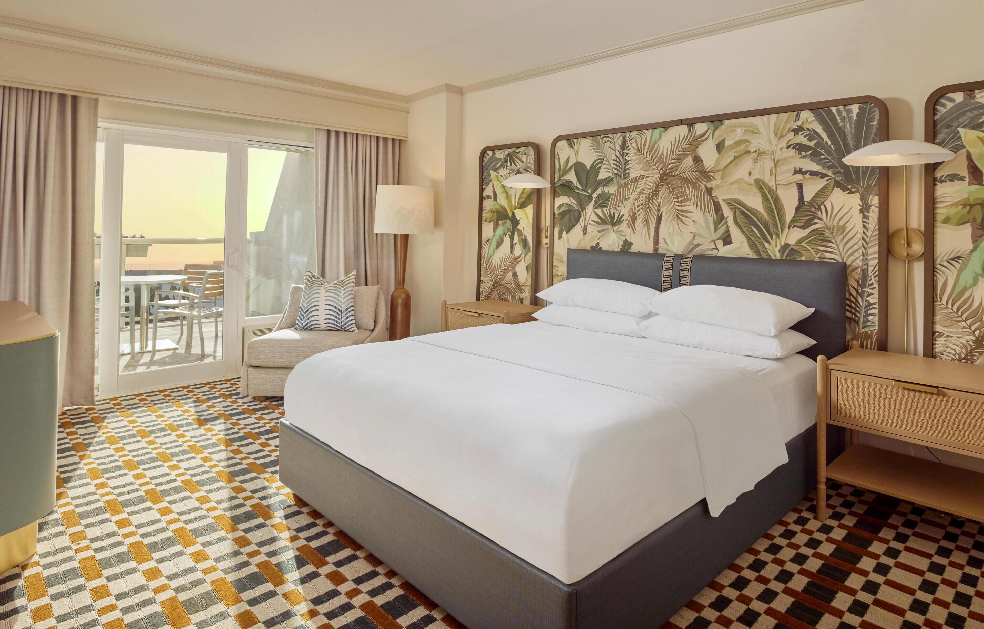 Habitación de hotel con una cama grande, un escritorio, una silla, una lámpara y vistas al exterior.