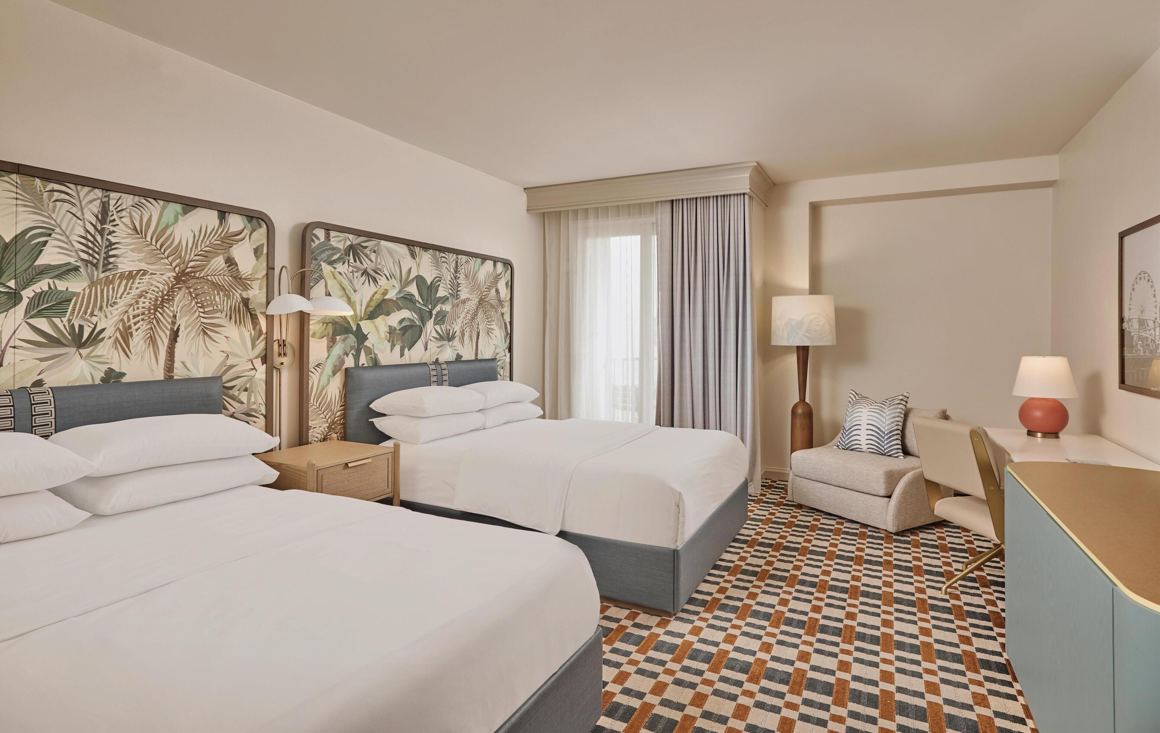 A hotel room with two beds, a desk, a chair, a lamp, and a window with curtains.