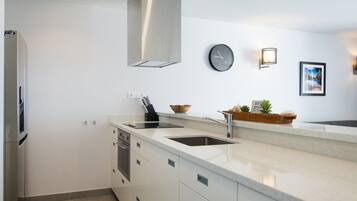 A modern kitchen with white cabinetry, a stainless steel refrigerator, a built-in oven, a sink, and a clock on the wall.