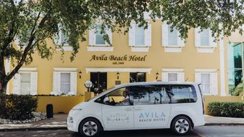 A white car parked in front of Avila Beach Hotel with a yellow facade and white shutters.