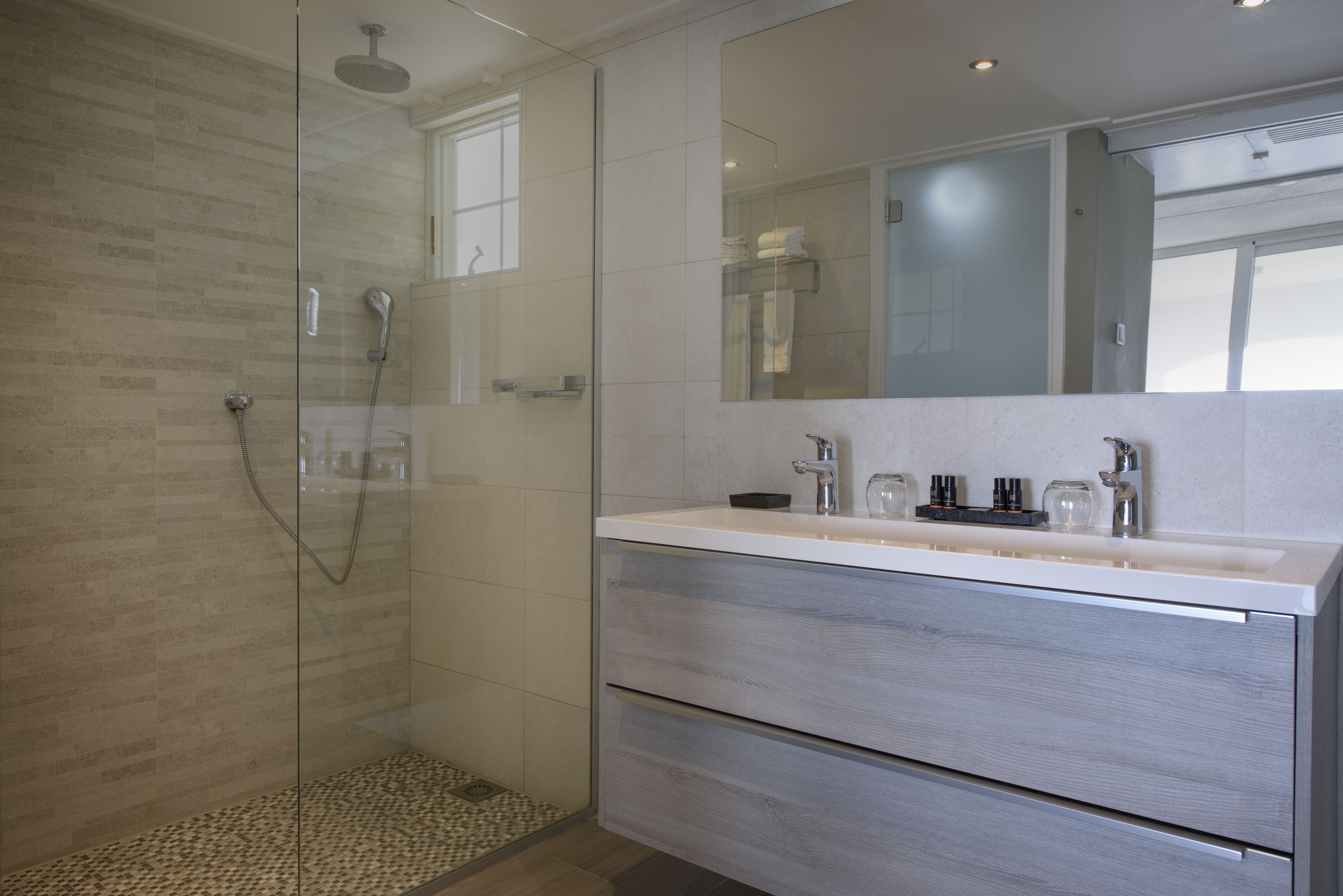 Un baño moderno con ducha envuelta en vidrio, un espejo grande y un tocador blanco con encimera.