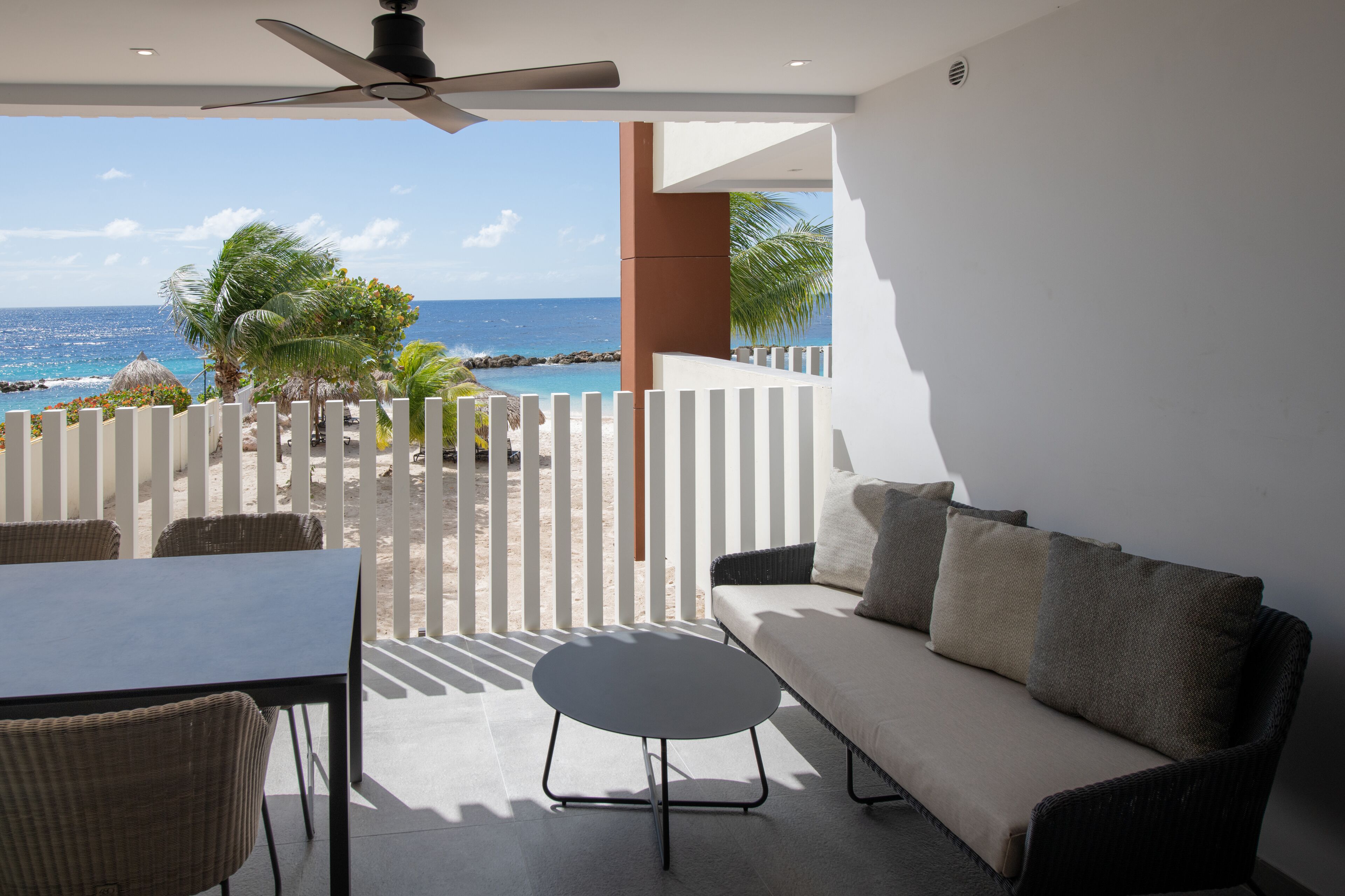 A modern balcony with a white fence, wicker furniture, and a view of the ocean.