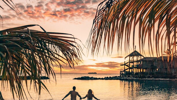 A beach scene with palm trees, a sunset, and a pier. - Avila Beach Hotel (Willemstad)