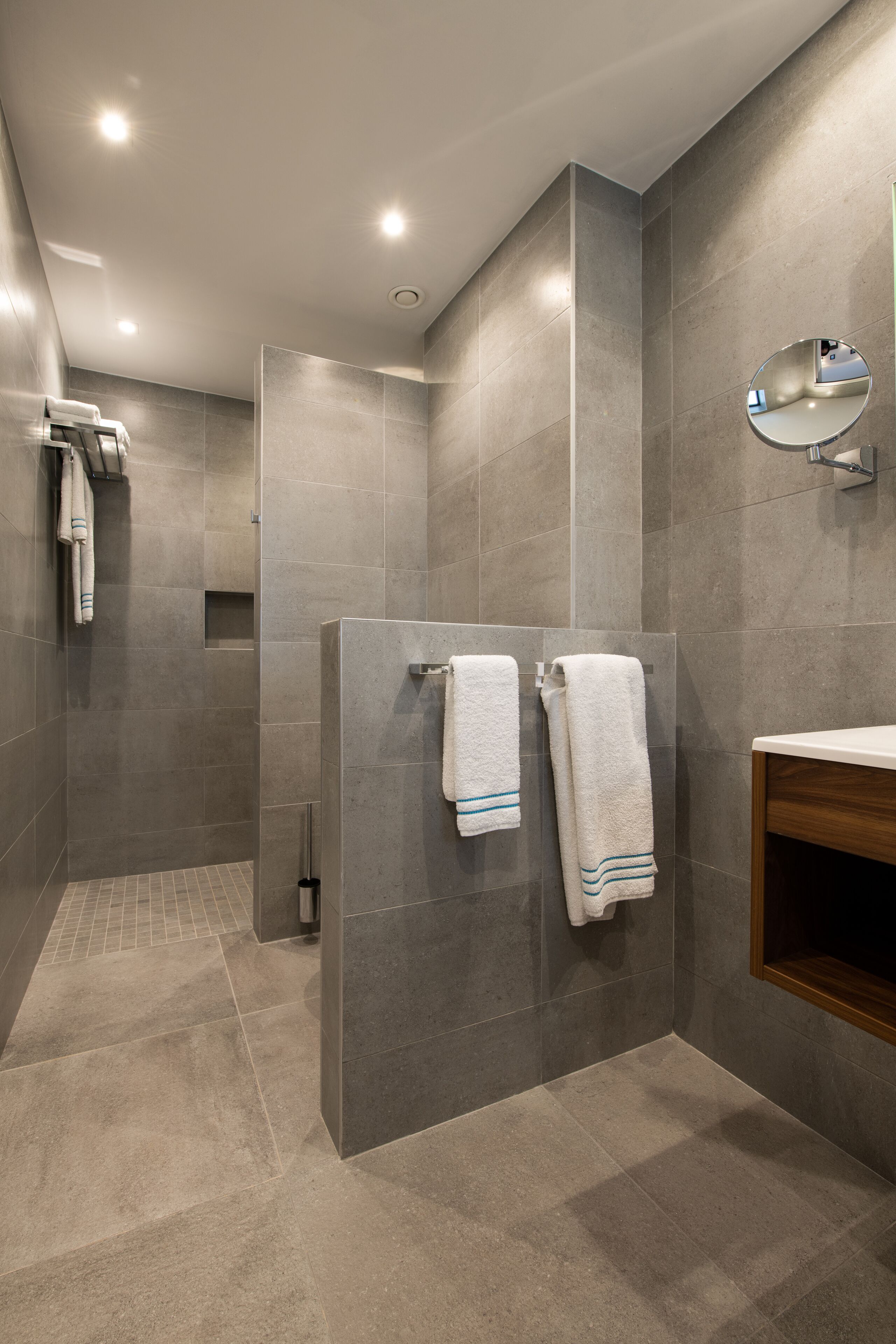 A modern bathroom with grey tiles, a wooden vanity, and two towels hanging on a wall-mounted rack.