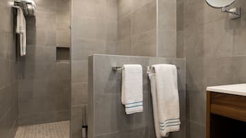 A modern bathroom with grey tiles, a wooden vanity, and two towels hanging on a wall-mounted rack.