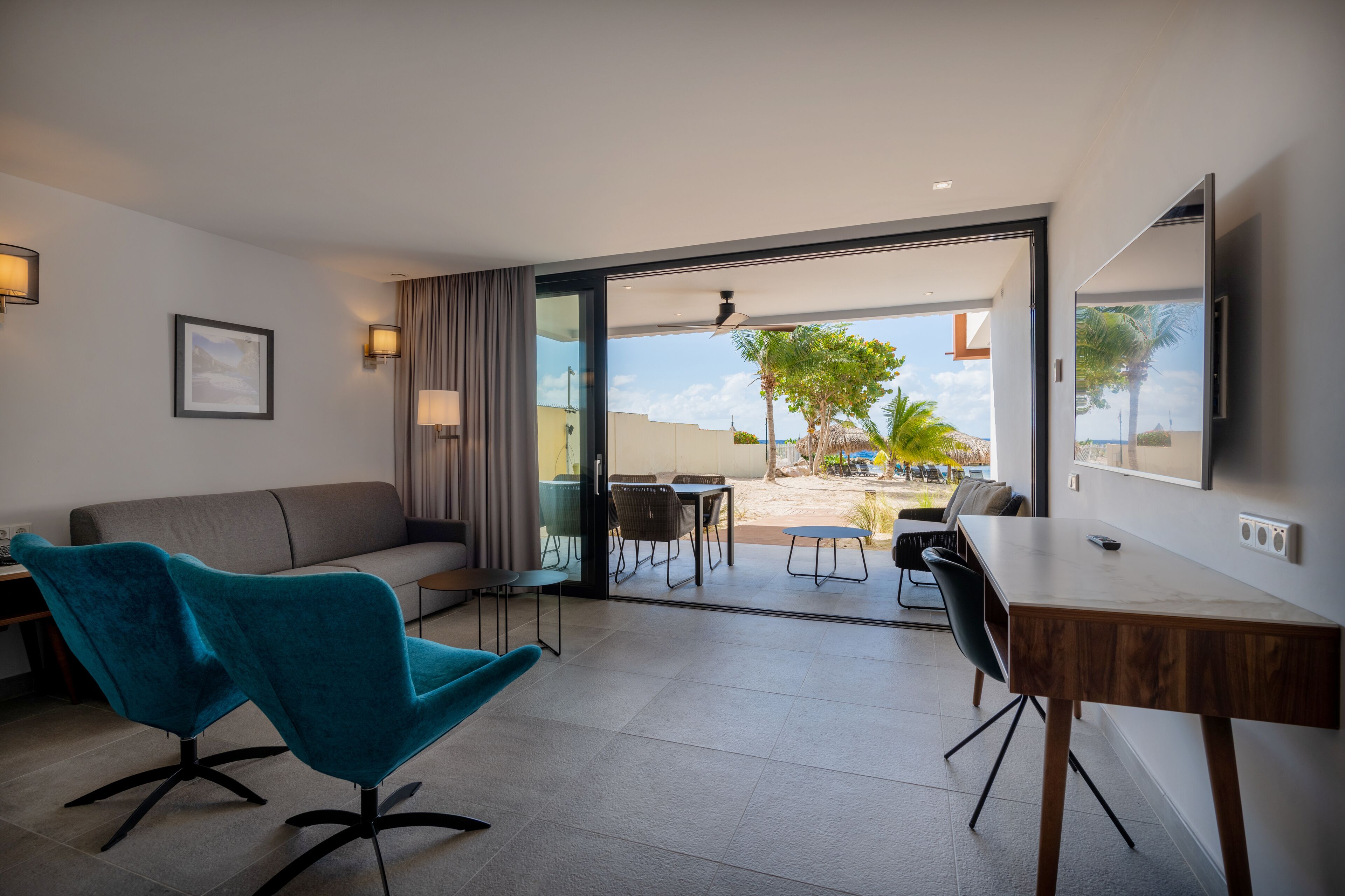 A modern living room with a sofa, a teal chair, a wooden desk, and a dining area.
