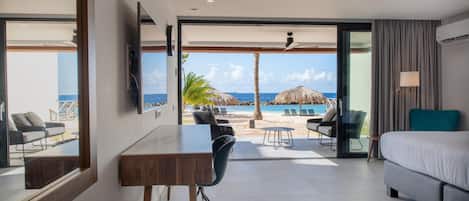 Habitación de hotel moderna con una cama grande, un escritorio y vistas a la playa y al océano.