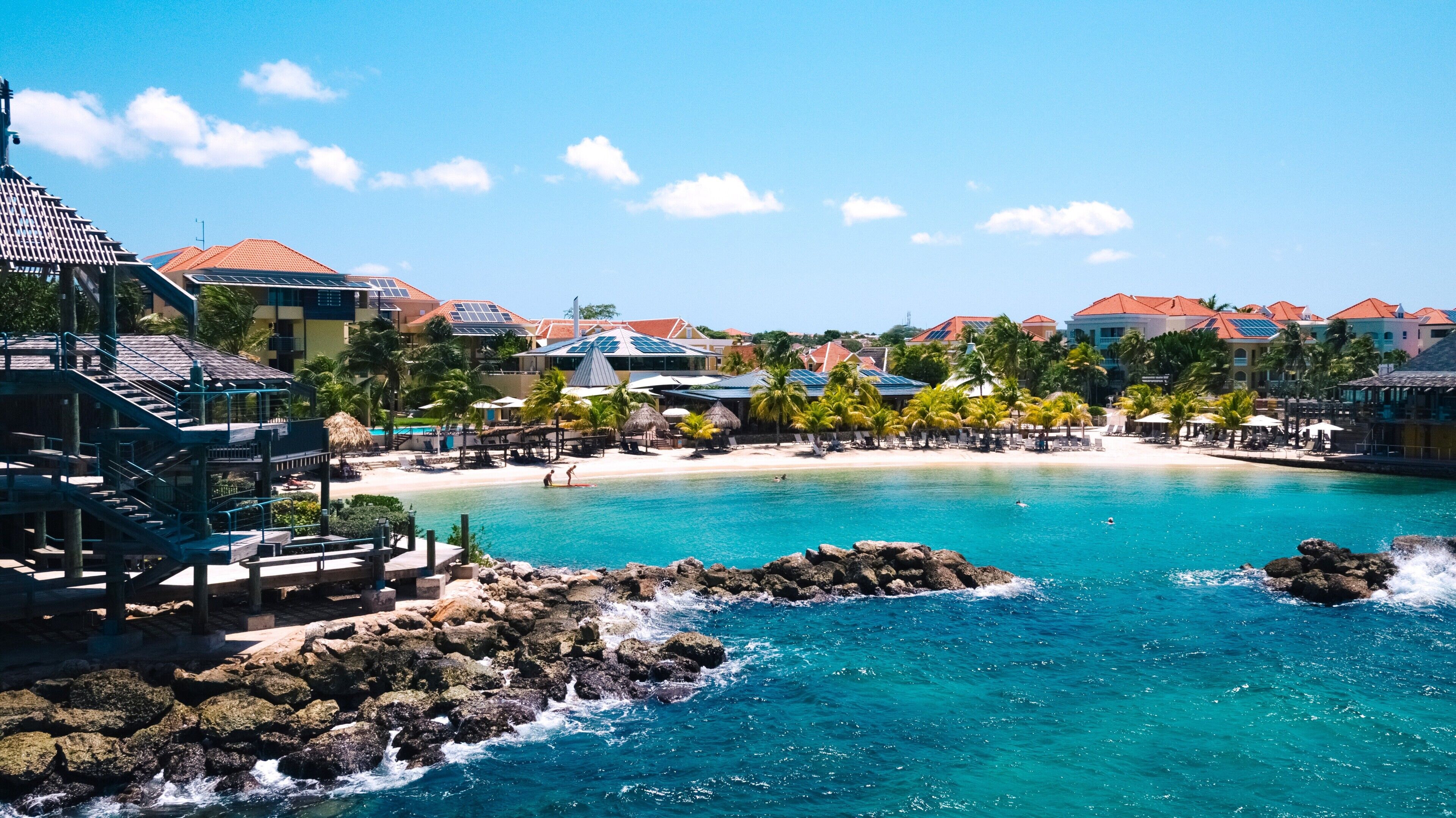 A resort with a swimming pool, beach, and buildings with red roofs.